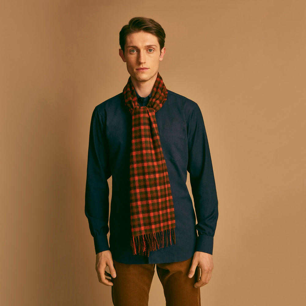 A man stands against a beige background wearing a navy long-sleeve shirt, brown pants, and a Turnbull & Asser Orange Multi Shepherd Check Cashmere Scarf draped around his neck. He faces forward with a neutral expression.
