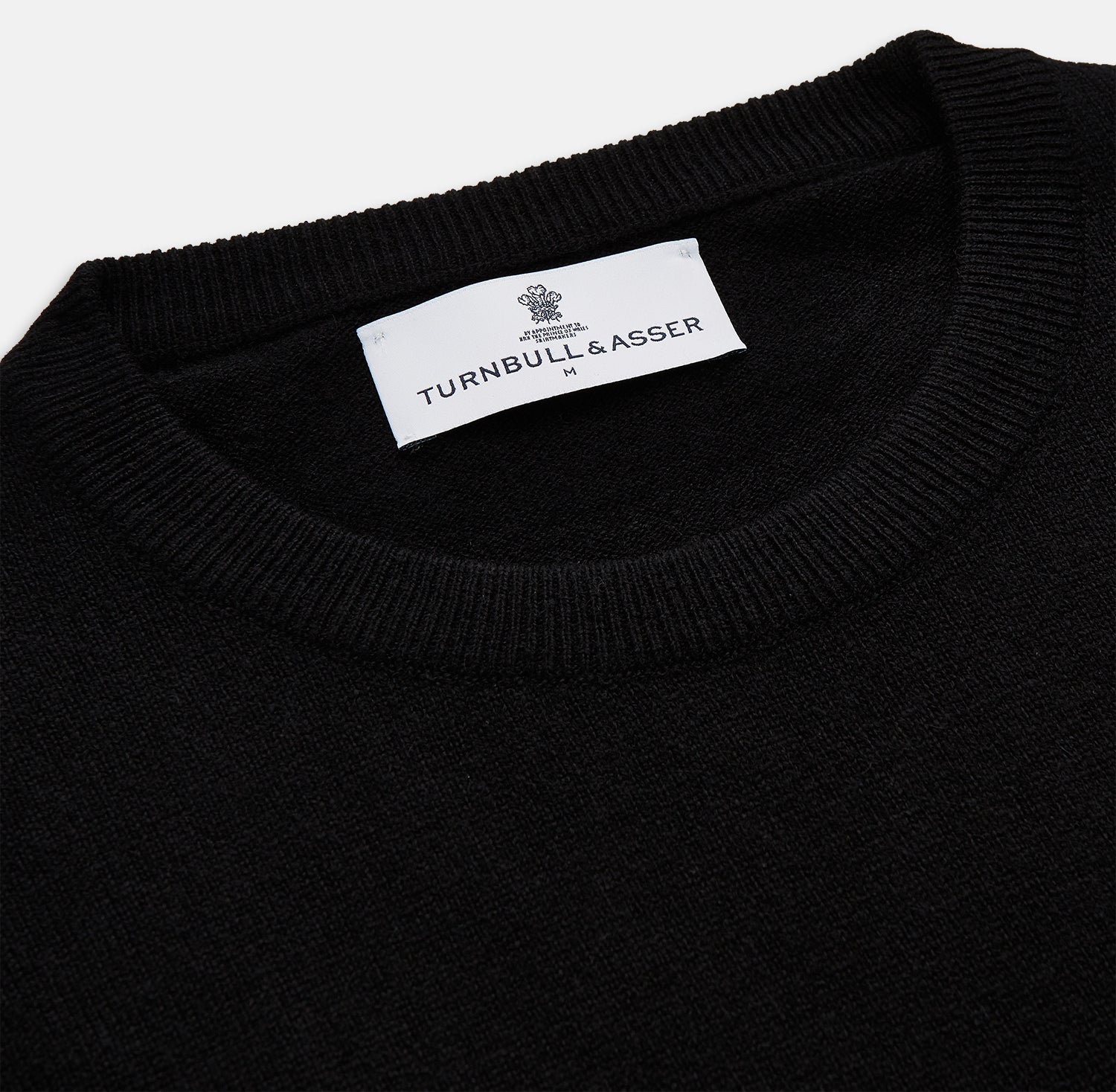 View 2 of product The Turnbull & Asser Black Crew Neck Cashmere Jumper is shown laid flat on a white background, featuring ribbed cuffs and hem with a small white label inside the collar.