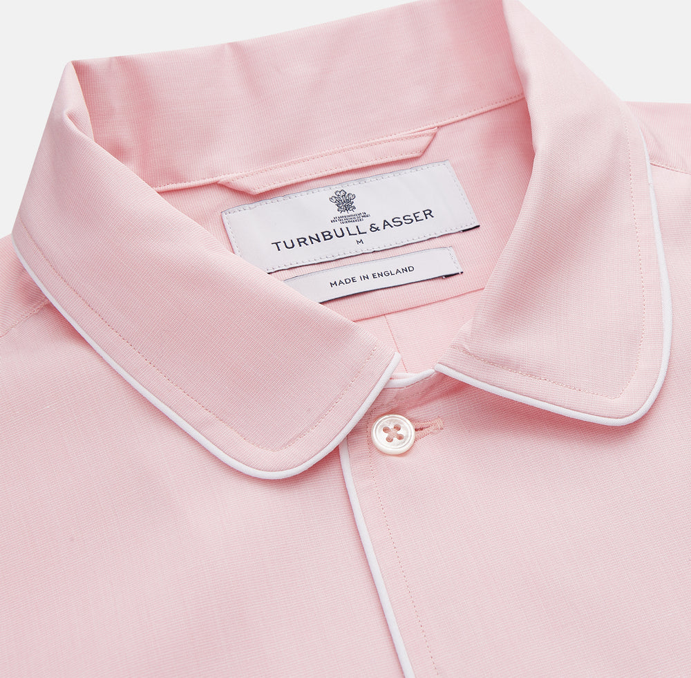 The Turnbull & Asser Pink Piped End-On-End Cotton Nightshirt features long sleeves, a pointed collar, button-down front, chest pocket, and a curved high-low hem for timeless, relaxed style.
