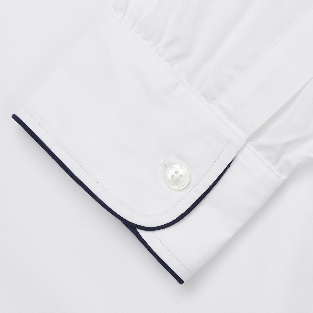 The Turnbull & Asser White Piped Cotton Nightshirt features black piping on the collar, chest pocket, and cuffs, plus a curved hem and loose-fitting sleeves gathered at the wrists for a classic look.