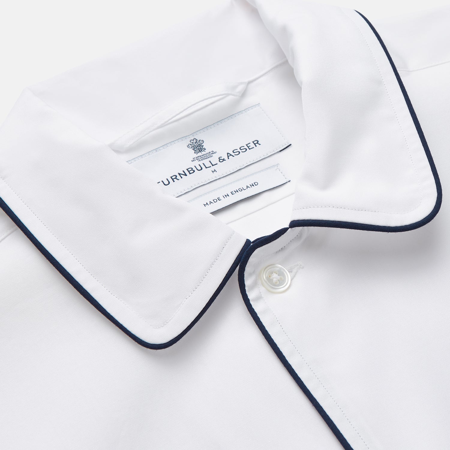 View 2 of product The Turnbull & Asser White Piped Cotton Nightshirt features black piping on the collar, chest pocket, and cuffs, plus a curved hem and loose-fitting sleeves gathered at the wrists for a classic look.