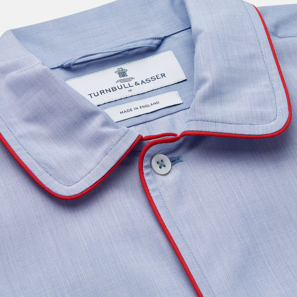 The Blue Piped End-on-End Cotton Nightshirt by Turnbull & Asser features light blue cotton, red piped accents, a chest pocket, high-low hem, and half-button placket—luxurious nightwear inspired by classic nightshirt style.
