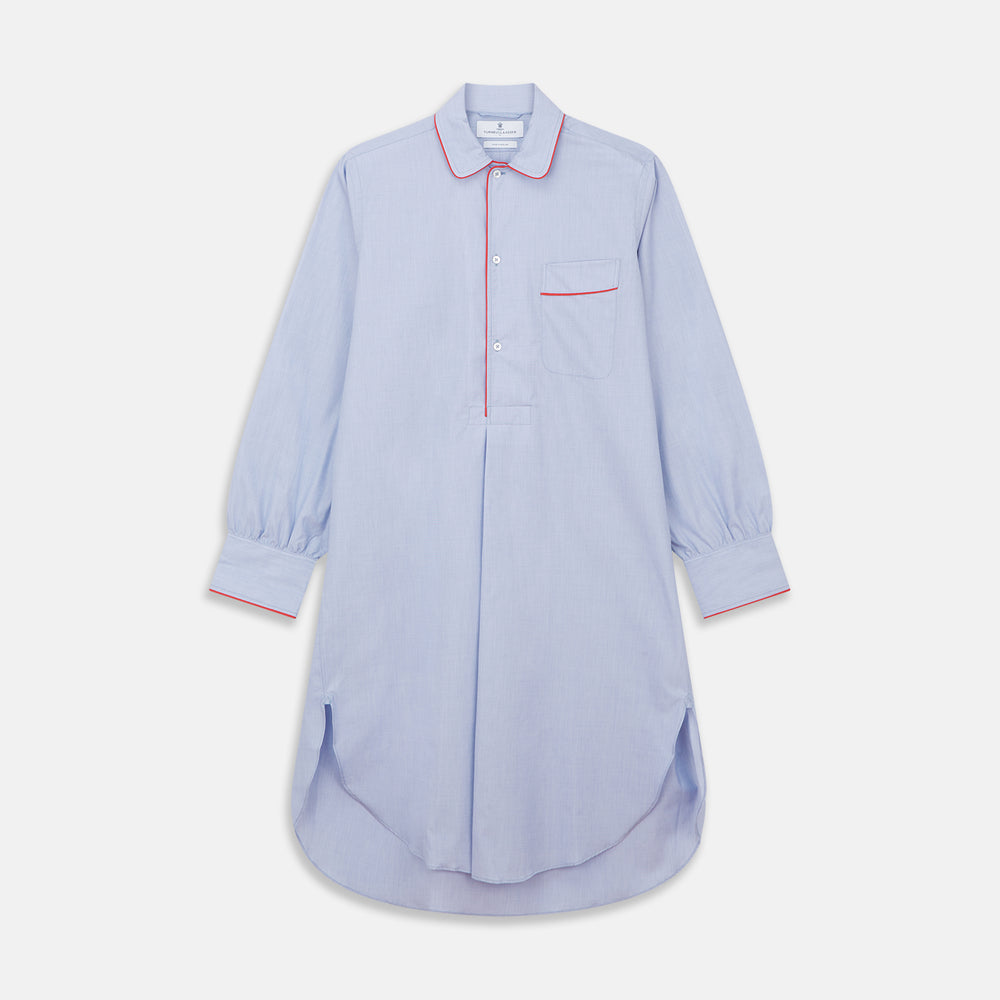 The Blue Piped End-on-End Cotton Nightshirt by Turnbull & Asser features light blue cotton, red piped accents, a chest pocket, high-low hem, and half-button placket—luxurious nightwear inspired by classic nightshirt style.