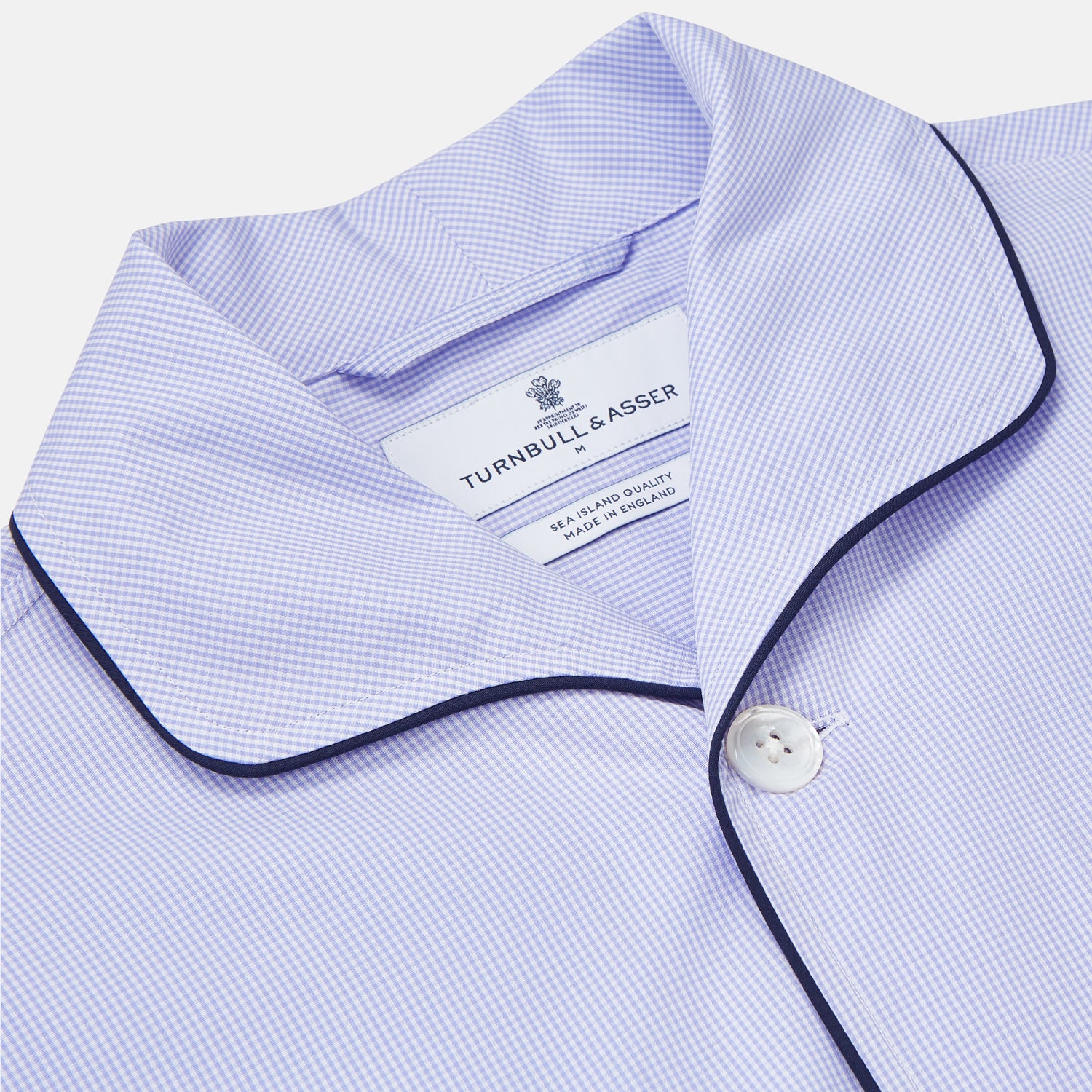 View 5 of product Turnbull & Asser's Blue Fine Check Piped Sea Island Quality Cotton Pyjama Set features white buttons, black piping on the collar, cuffs, and pocket, with matching drawstring pants—displayed flat on a white background.