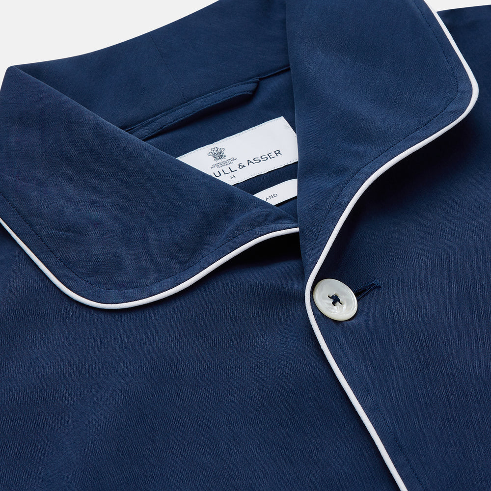 The Turnbull & Asser Navy Piped Silk Pyjama Set features a long-sleeve button-up top with a chest pocket and matching drawstring pants, laid flat on a white background for a luxurious look.