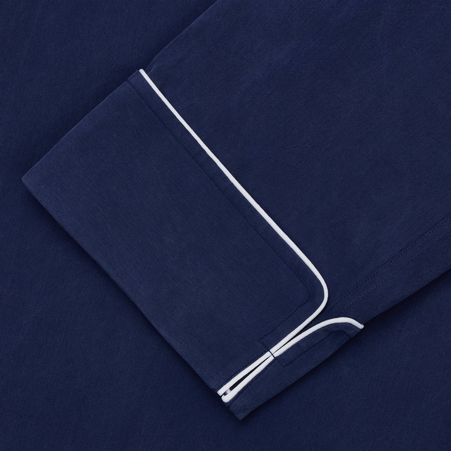 View 4 of product The Turnbull & Asser Navy Piped Silk Pyjama Set features a long-sleeve button-up top with a chest pocket and matching drawstring pants, laid flat on a white background for a luxurious look.