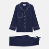 View 2 of product The Women's Harriet Navy Silk Pyjama Set by Turnbull & Asser features a long-sleeve, button-up top with white piping and chest pocket, plus matching drawstring pants—luxurious sleepwear displayed on a white background.