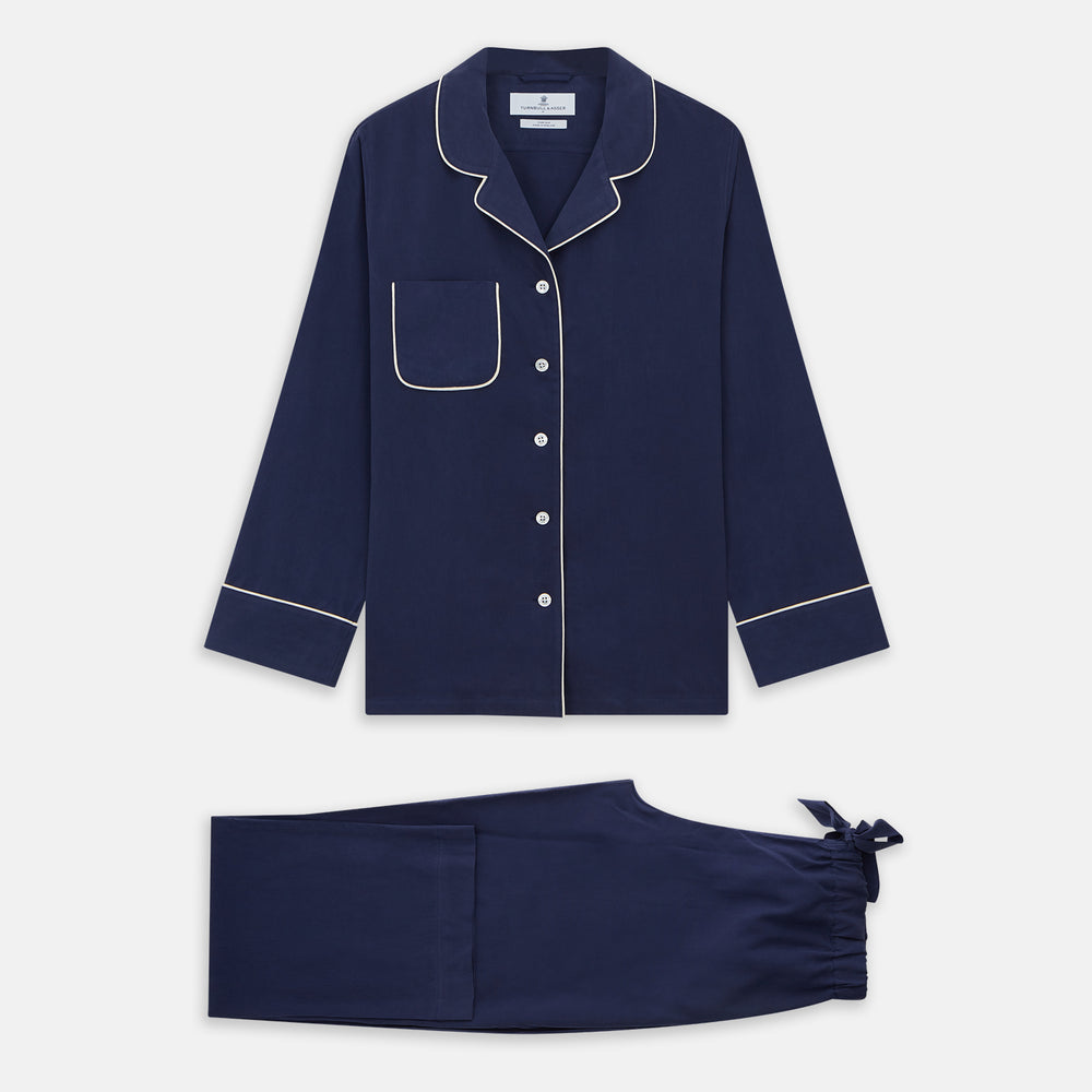 The Women's Harriet Navy Silk Pyjama Set by Turnbull & Asser features a long-sleeve, button-up top with white piping and chest pocket, plus matching drawstring pants—luxurious sleepwear displayed on a white background.