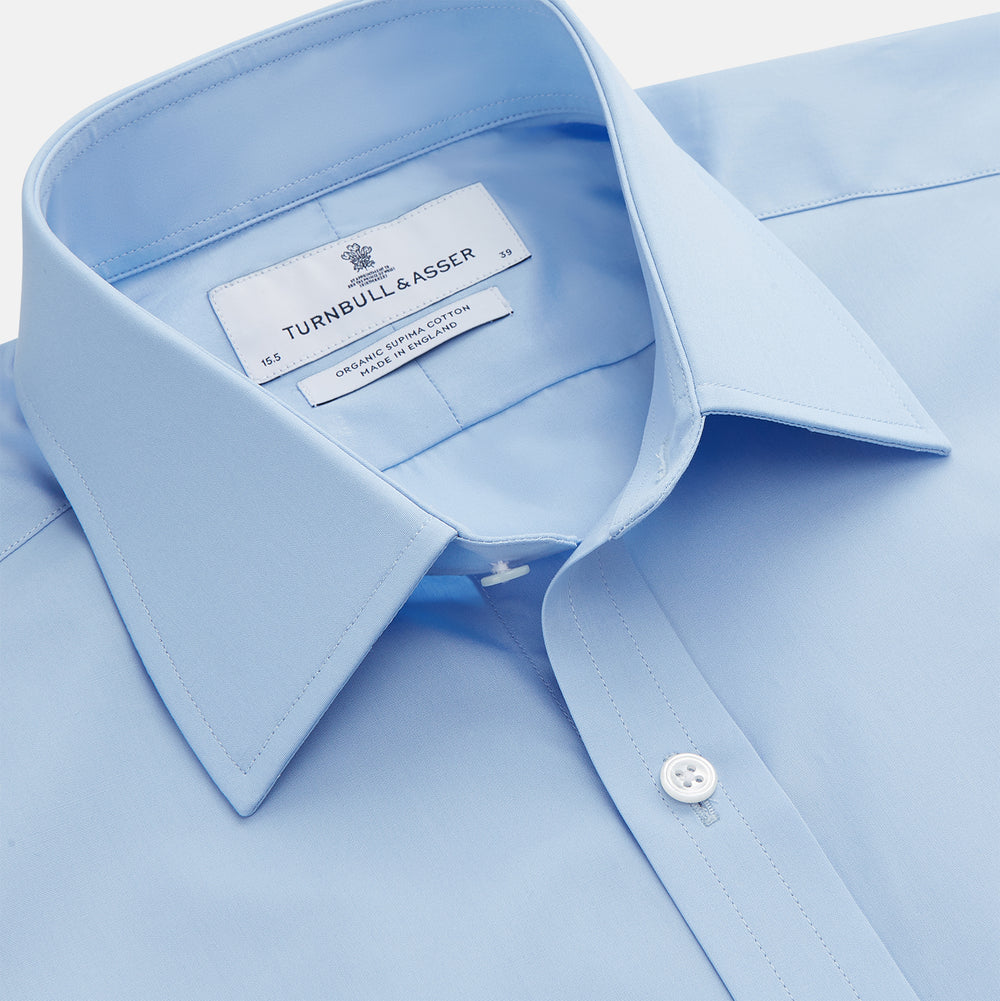 The Turnbull & Asser Pale Blue Organic Cotton Regular Fit Mayfair Shirt features long sleeves, a pointed collar, white buttons, and buttoned cuffs, shown laid flat on a white background.