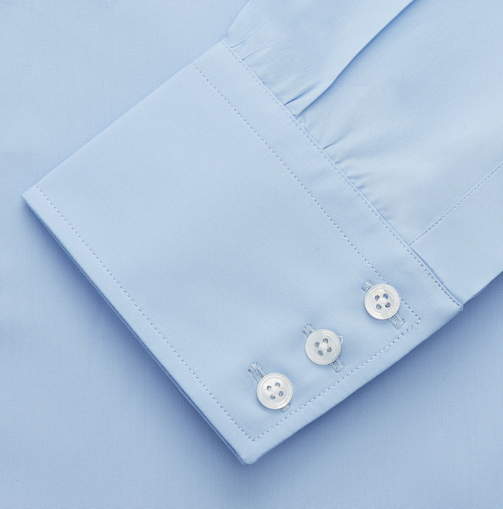 The Turnbull & Asser Pale Blue Organic Cotton Regular Fit Mayfair Shirt features long sleeves, a pointed collar, white buttons, and buttoned cuffs, shown laid flat on a white background.