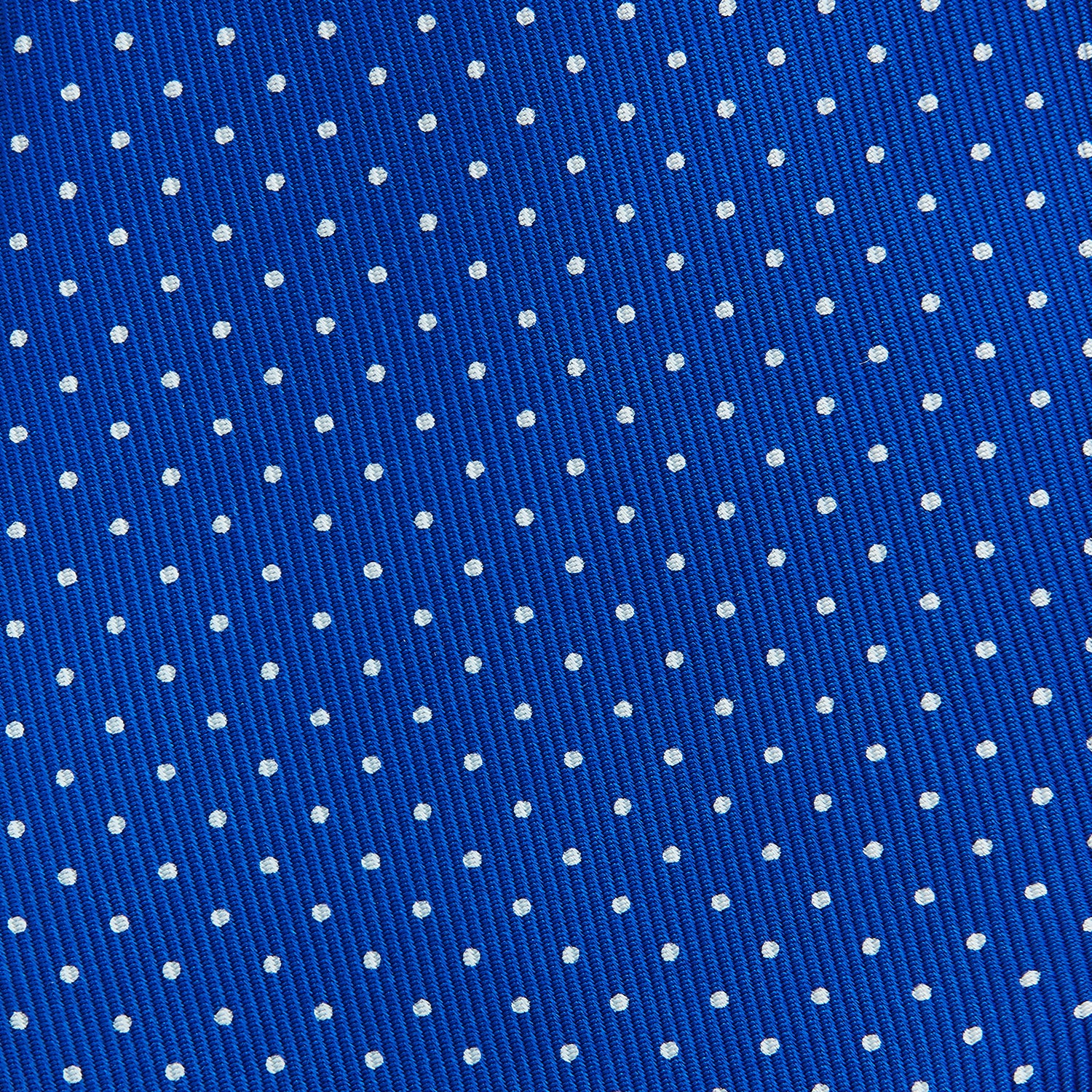 View 3 of product The Turnbull & Asser Long Blue and White Small Spot Printed Silk Tie, featuring white polka dots on royal blue silk, is shown rolled up on a plain white background.