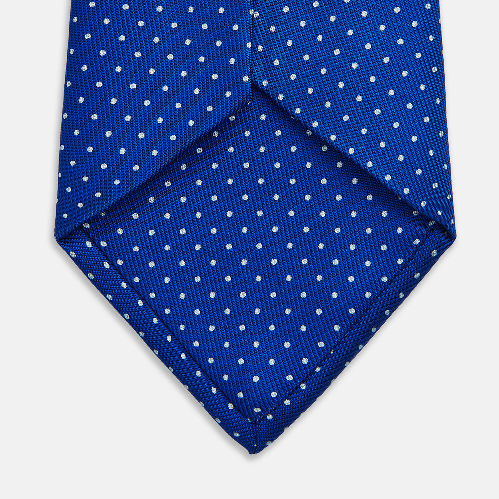 The Turnbull & Asser Long Blue and White Small Spot Printed Silk Tie, featuring white polka dots on royal blue silk, is shown rolled up on a plain white background.