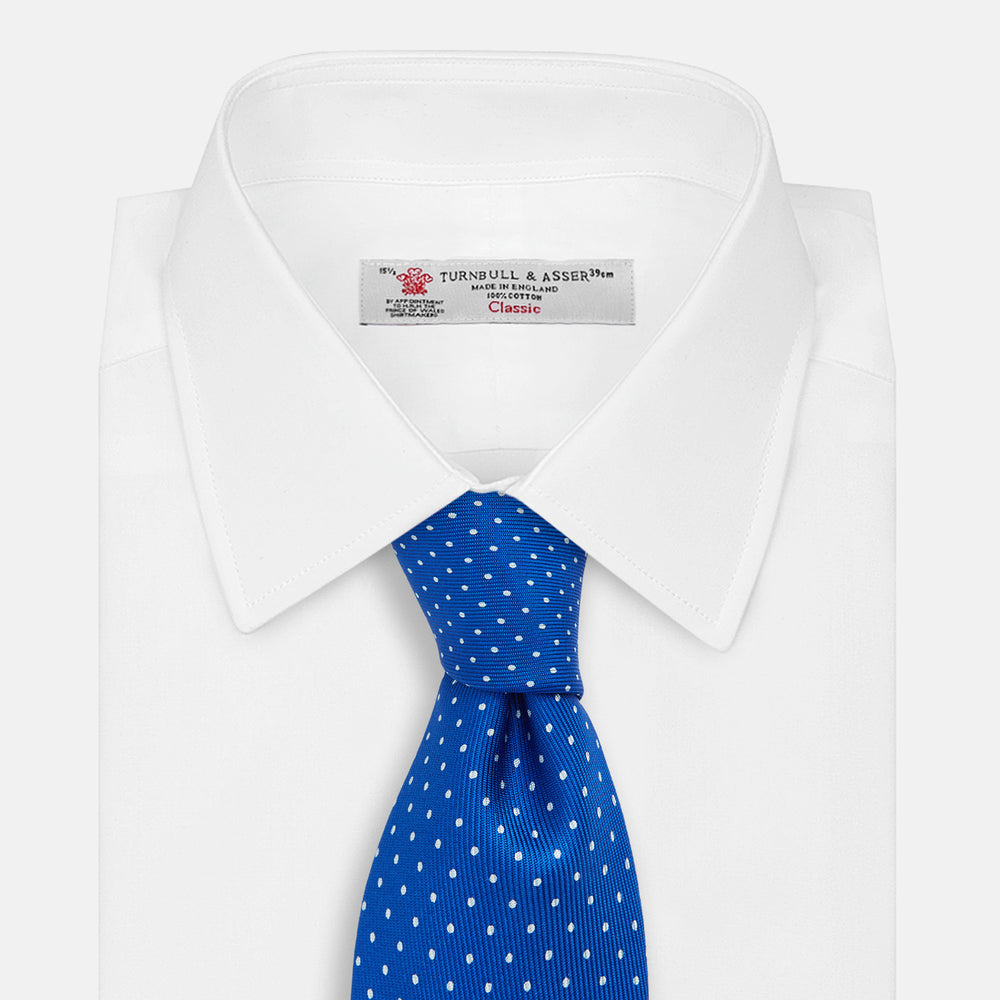 The Turnbull & Asser Long Blue and White Small Spot Printed Silk Tie, featuring white polka dots on royal blue silk, is shown rolled up on a plain white background.
