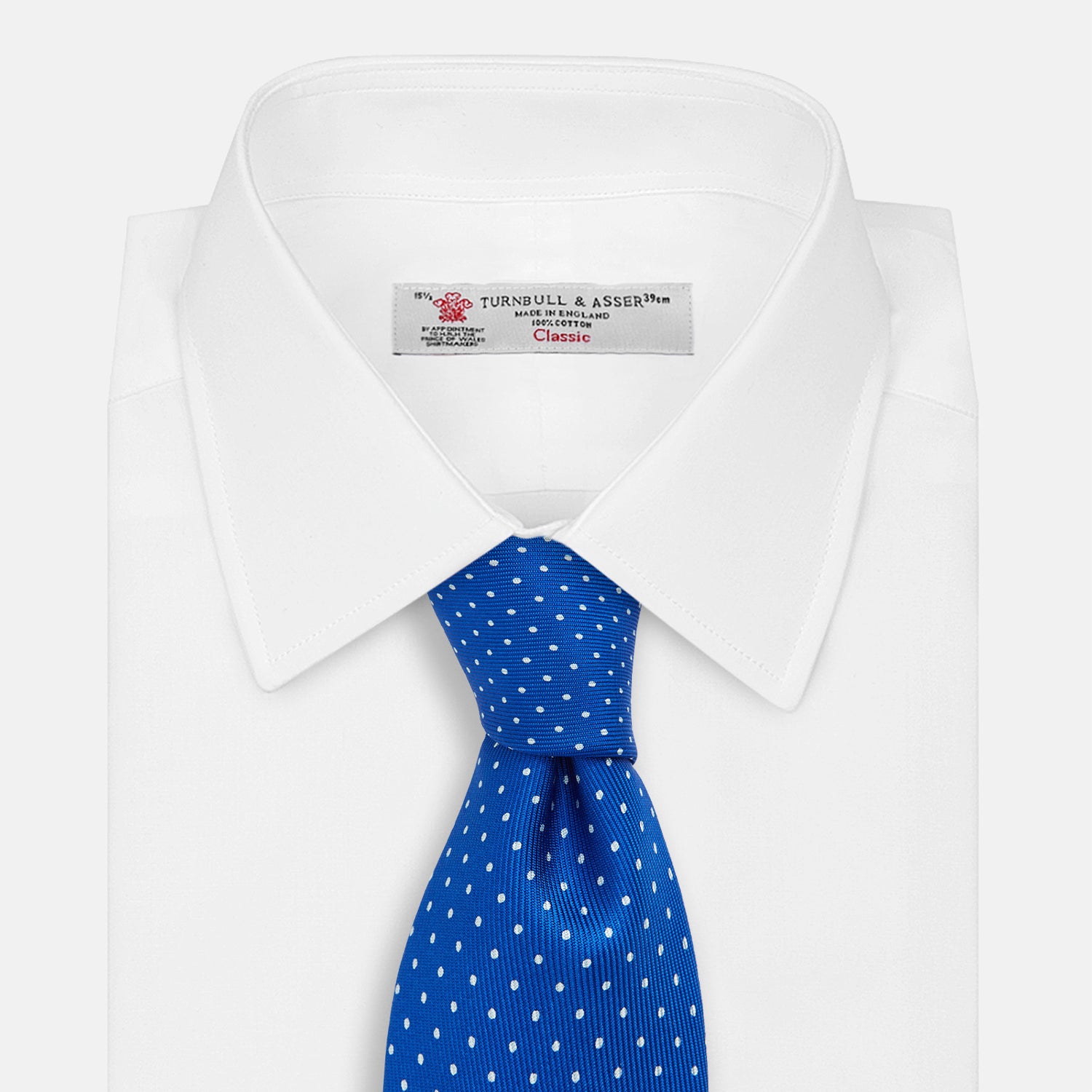 View 2 of product The Turnbull & Asser Long Blue and White Small Spot Printed Silk Tie, featuring white polka dots on royal blue silk, is shown rolled up on a plain white background.