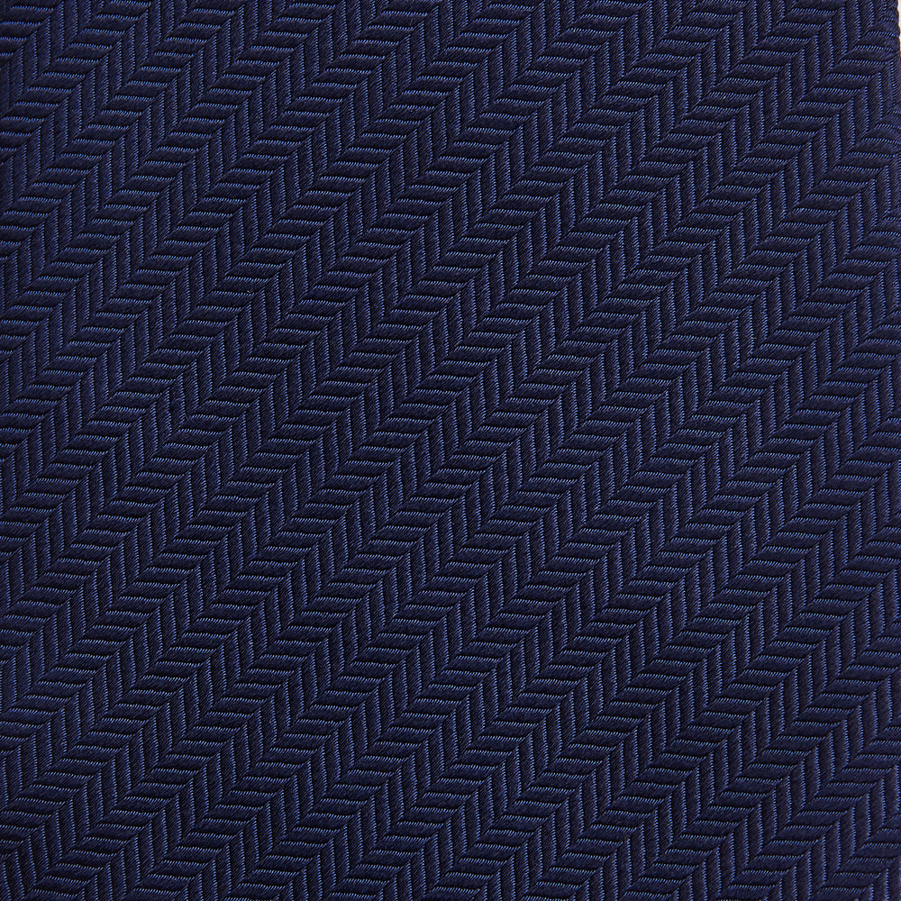 The Long Navy Herringbone Silk Tie by Turnbull & Asser is shown rolled up on a plain white background, highlighting its subtle herringbone weave and luxurious silk fabric.