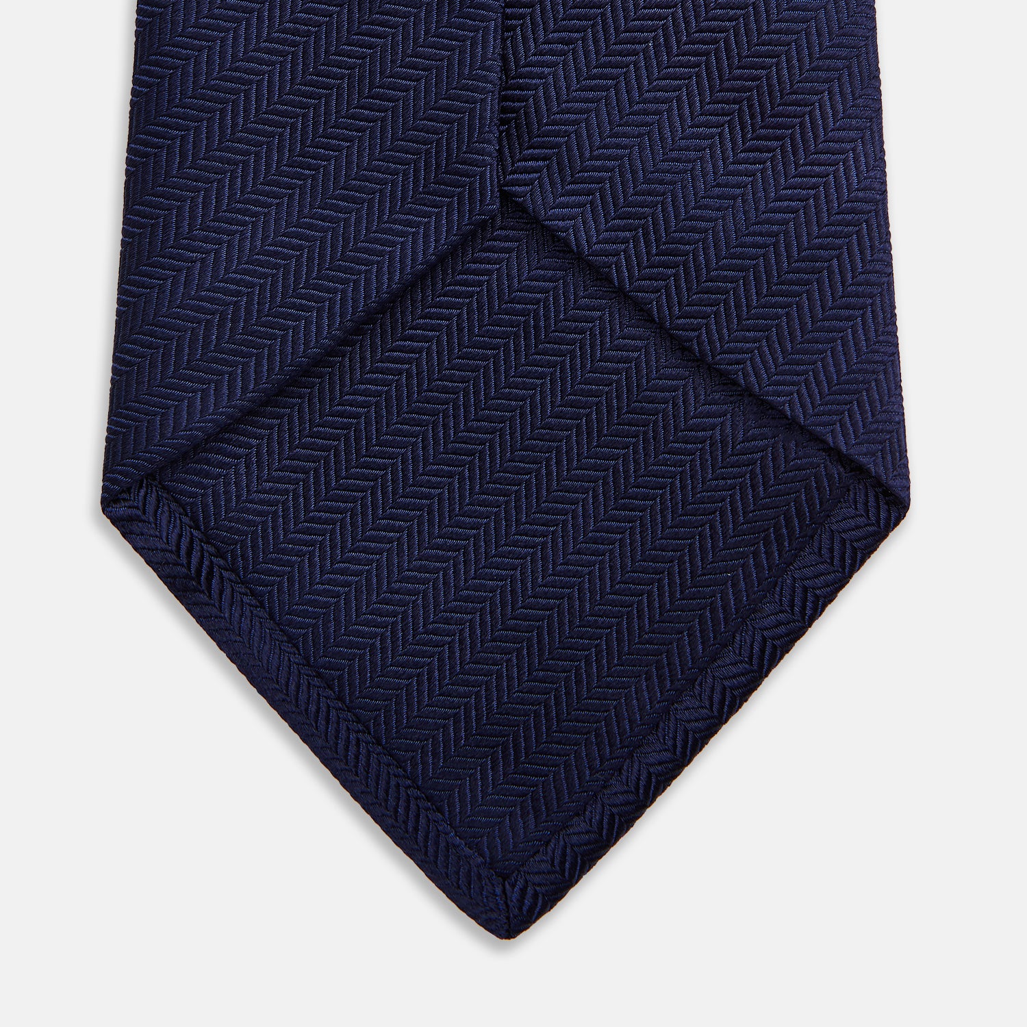 View 4 of product The Long Navy Herringbone Silk Tie by Turnbull & Asser is shown rolled up on a plain white background, highlighting its subtle herringbone weave and luxurious silk fabric.