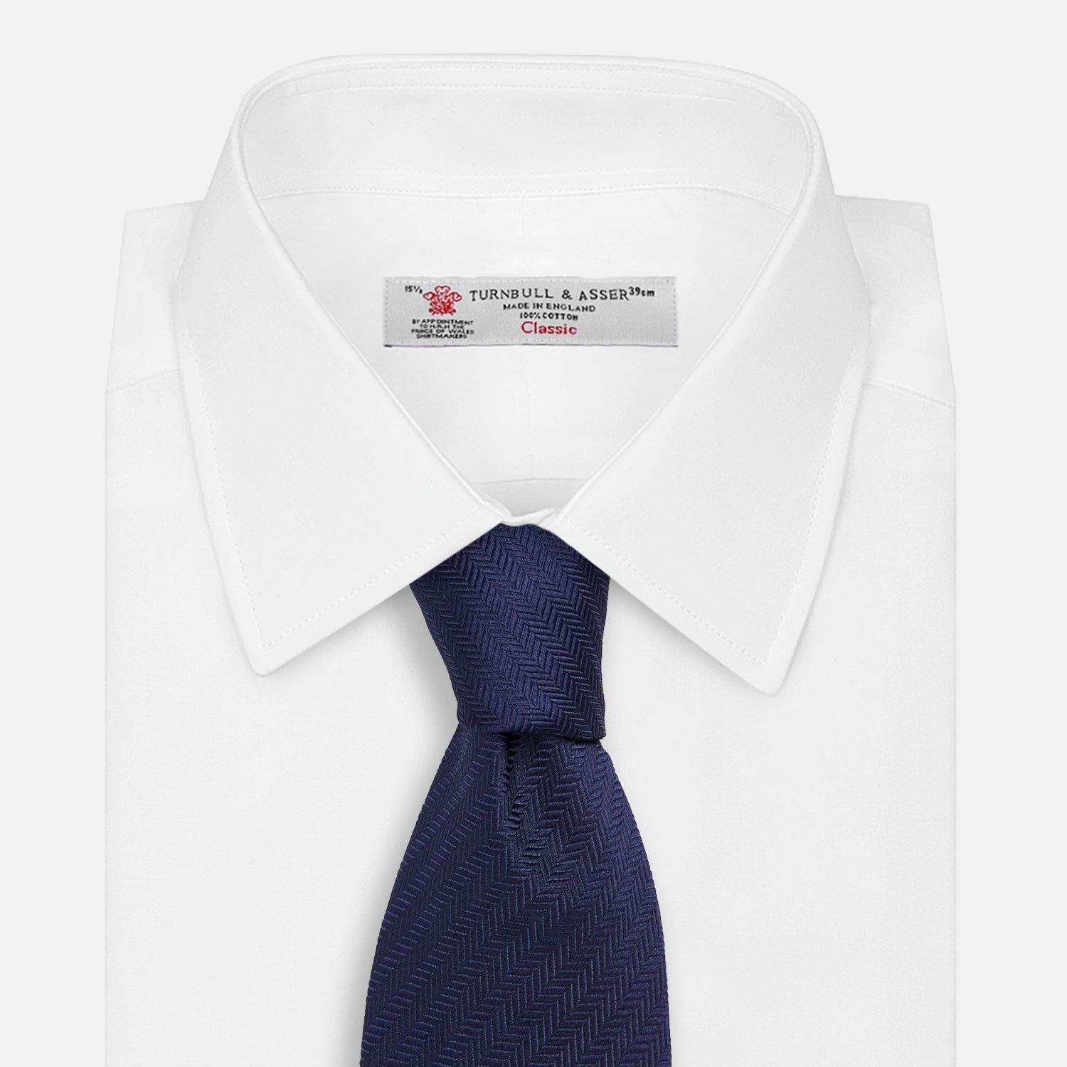 View 2 of product The Long Navy Herringbone Silk Tie by Turnbull & Asser is shown rolled up on a plain white background, highlighting its subtle herringbone weave and luxurious silk fabric.
