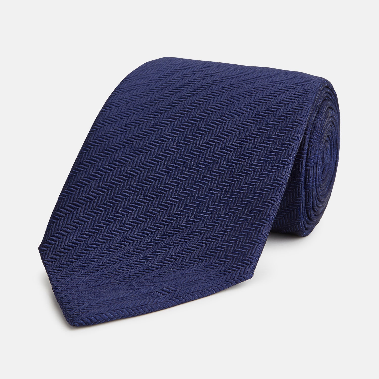 View 1 of product The Long Navy Herringbone Silk Tie by Turnbull & Asser is shown rolled up on a plain white background, highlighting its subtle herringbone weave and luxurious silk fabric.