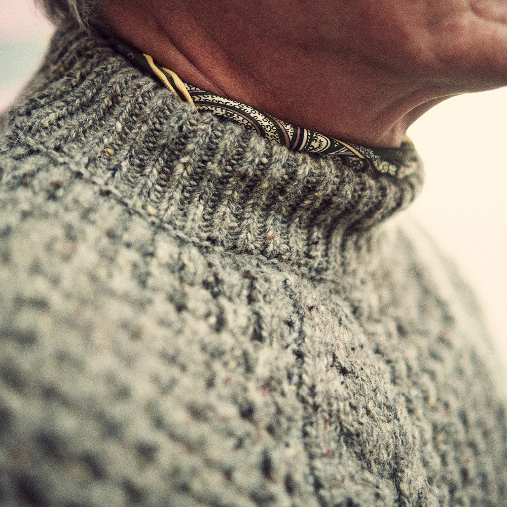 The Turnbull & Asser Merino Knitted Raglan Sleeve Crewneck Jumper in gray features intricate front and sleeve knit patterns, a high neckline, and long sleeves—an essential piece of men’s knitwear. Laid flat on a white background.