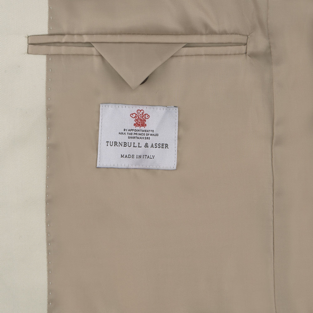 The Turnbull & Asser Stone Cotton Twill Jacket features a notch lapel, chest pocket, two front flap pockets, and brown buttons. Italian-tailored for smart-casual style, it is shown here against a white background.