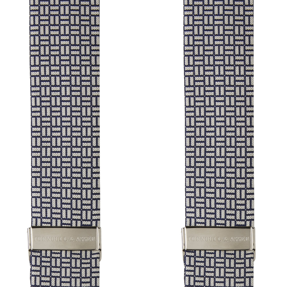 Turnbull & Asser’s Silver and Charcoal Geometric Adjustable Silk Braces feature a black and white geometric pattern, black leather looped ends, and metal hardware, echoing classic refinement against a plain white background.