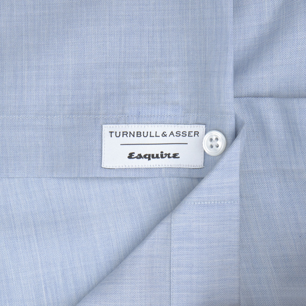 The Turnbull & Asser Esquire Edit Tailored Fit Light Blue Shirt features a Kent collar and 2-button cuffs, neatly folded and displayed on a plain light gray background.