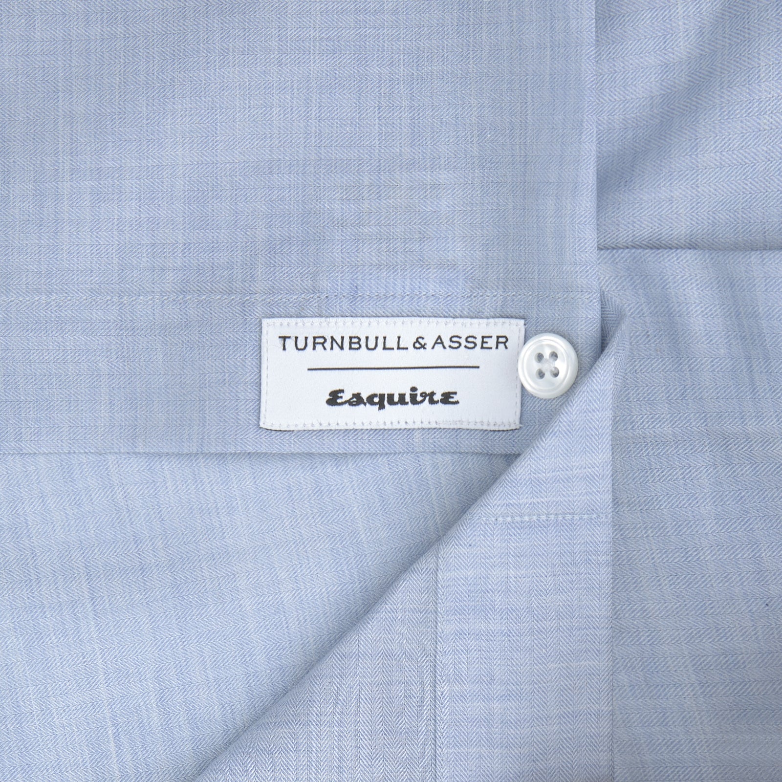 View 2 of product The Turnbull & Asser Esquire Edit Tailored Fit Light Blue Shirt features a Kent collar and 2-button cuffs, neatly folded and displayed on a plain light gray background.