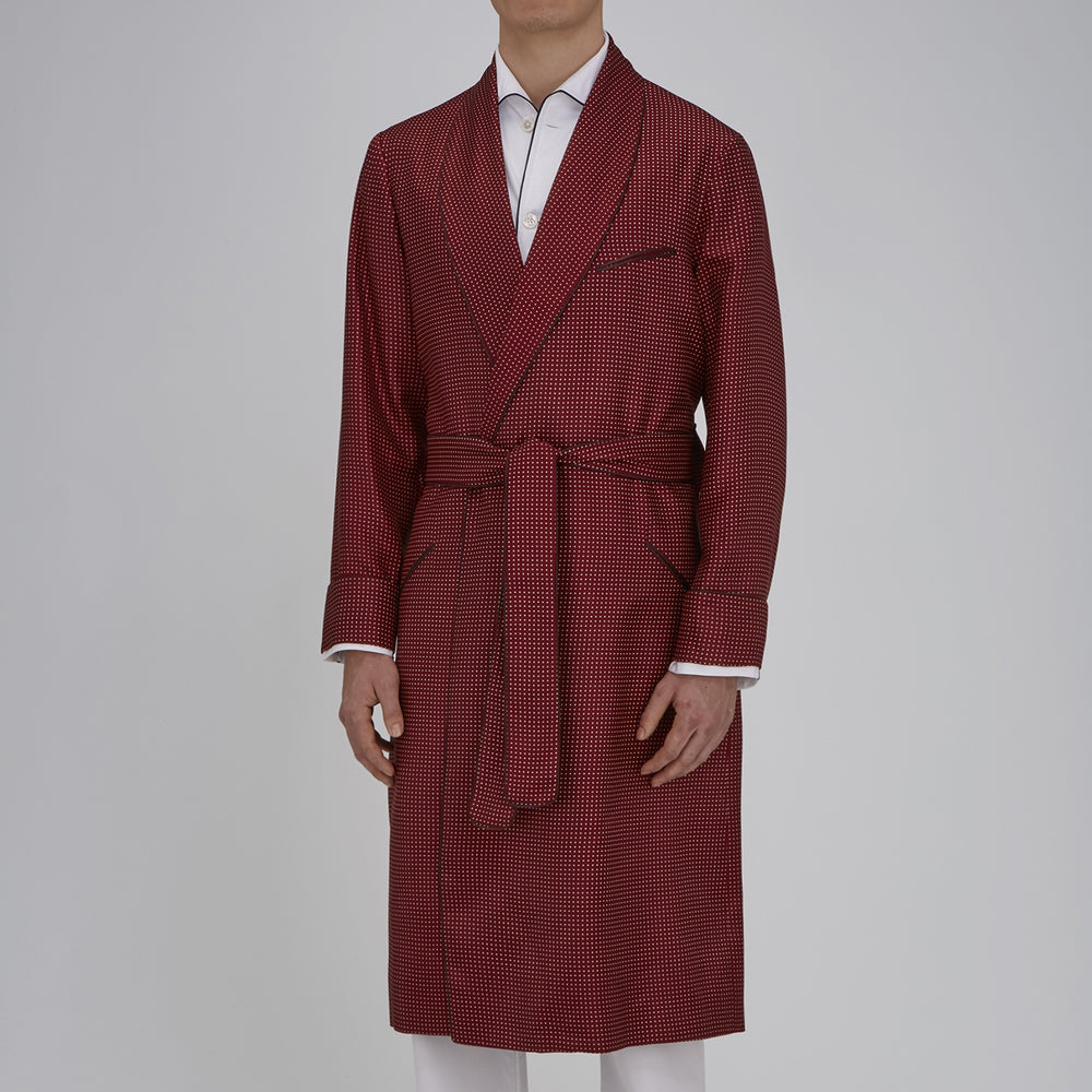 The Turnbull & Asser Burgundy Piped Silk Spot Gown features small white polka dots, a shawl collar, fabric belt, and chest pocket—luxurious nightwear and a stylish men’s statement piece—shown on a white background.