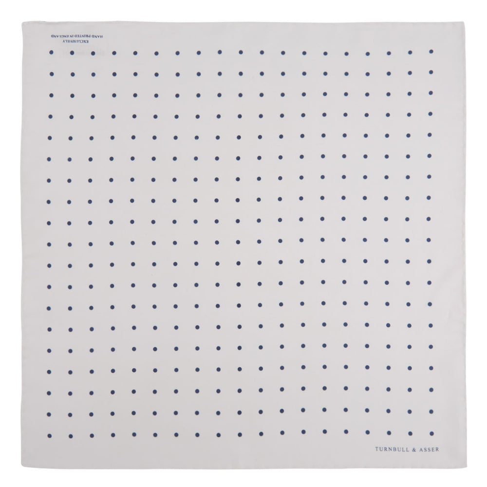 The White and Navy Spot Silk Pocket Square by Turnbull & Asser features evenly spaced blue dots and the brand's logo in blue on the bottom right, with a folded corner highlighting this classic men's accessory.