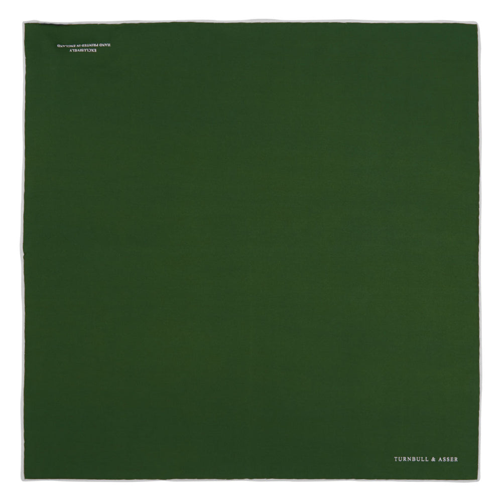 The Olive and White Piped Silk Pocket Square by Turnbull & Asser features a subtle white border and the brand’s embroidered logo—a timeless accessory for any occasion.