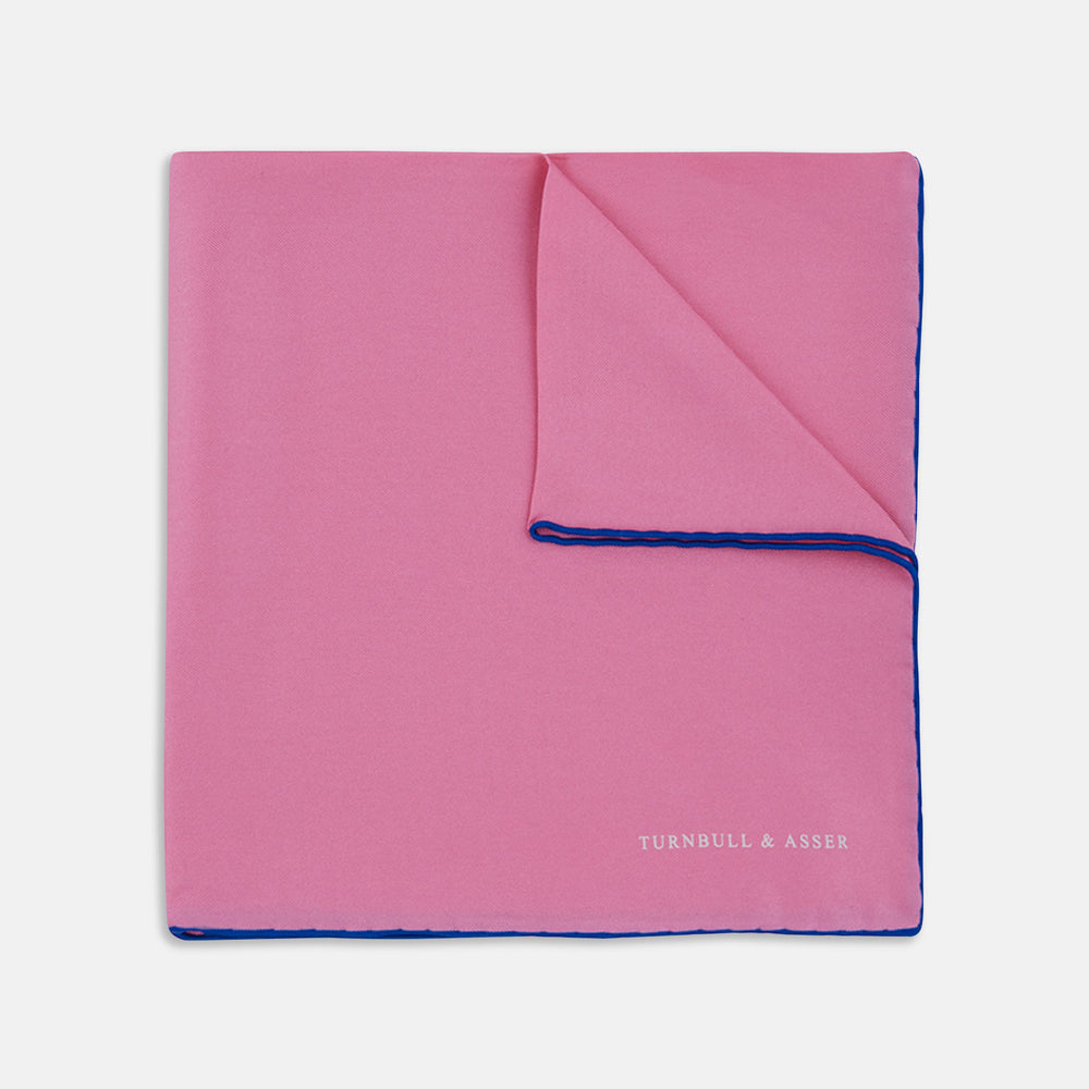 The Rose and Navy Piped Silk Pocket Square by Turnbull & Asser features classic pink silk with navy edging, neatly folded to display both sides. Turnbull & Asser’s logo appears in white on the lower right corner for a refined finish.