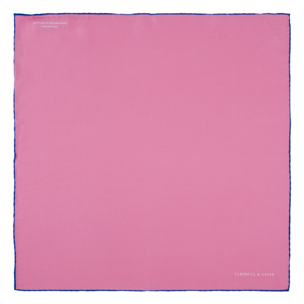 The Rose and Navy Piped Silk Pocket Square by Turnbull & Asser features classic pink silk with navy edging, neatly folded to display both sides. Turnbull & Asser’s logo appears in white on the lower right corner for a refined finish.
