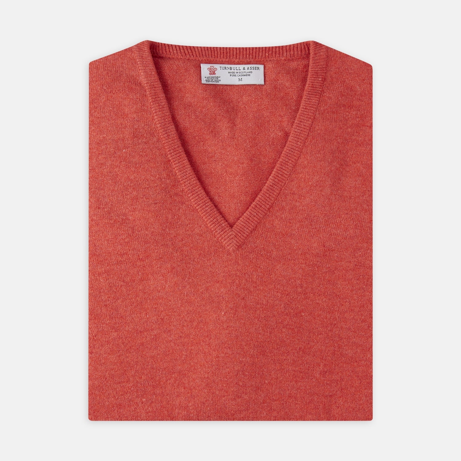 View 1 of product A folded Crimson Fine Cashmere Slipover by Turnbull & Asser in coral-red is shown against a white background, with the visible neckline label highlighting its premium Scottish cashmere quality.