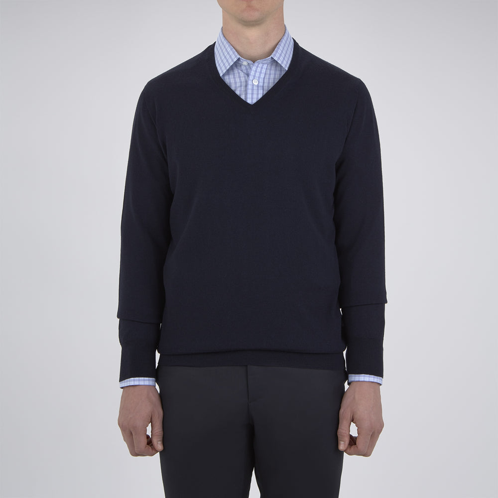 The Turnbull & Asser Indigo V-Neck Merino Wool Jumper, shown neatly folded with ribbed cuffs and a visible inner label, is a timeless essential in versatile navy, perfect for any gentleman’s wardrobe.