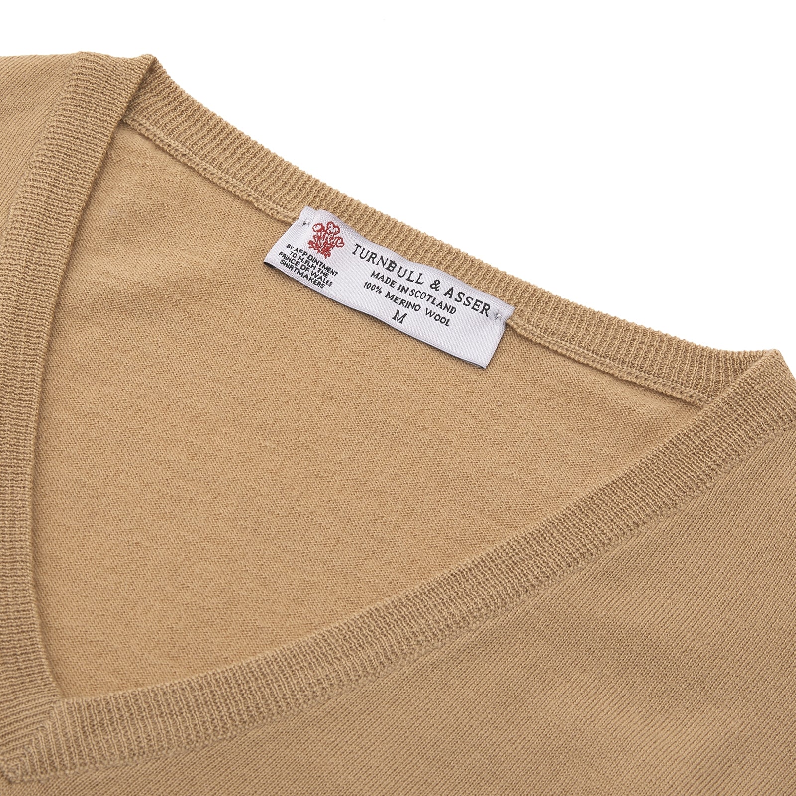 View 4 of product The Turnbull & Asser Camel V-Neck Merino Wool Jumper, with ribbed cuffs and a visible white neckline label, is neatly folded with one sleeve showing—an essential, versatile staple for any gentleman's wardrobe.