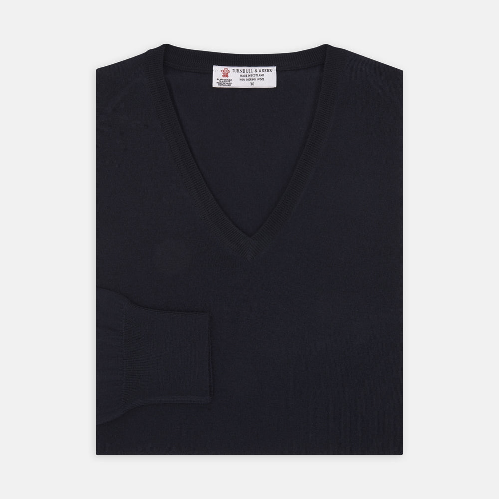 The Turnbull & Asser Indigo V-Neck Merino Wool Jumper, shown neatly folded with ribbed cuffs and a visible inner label, is a timeless essential in versatile navy, perfect for any gentleman’s wardrobe.