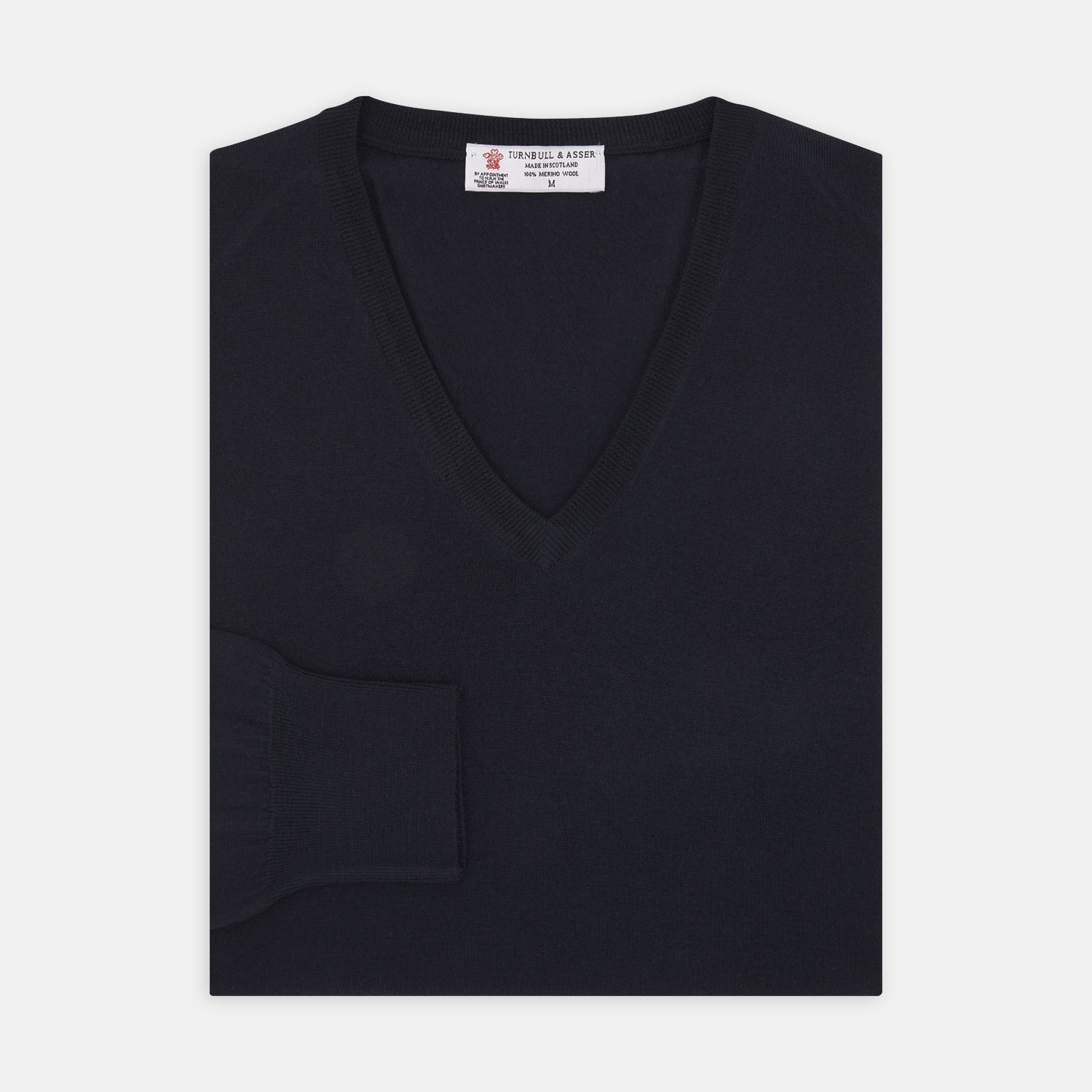 View 1 of product The Turnbull & Asser Indigo V-Neck Merino Wool Jumper, shown neatly folded with ribbed cuffs and a visible inner label, is a timeless essential in versatile navy, perfect for any gentleman’s wardrobe.