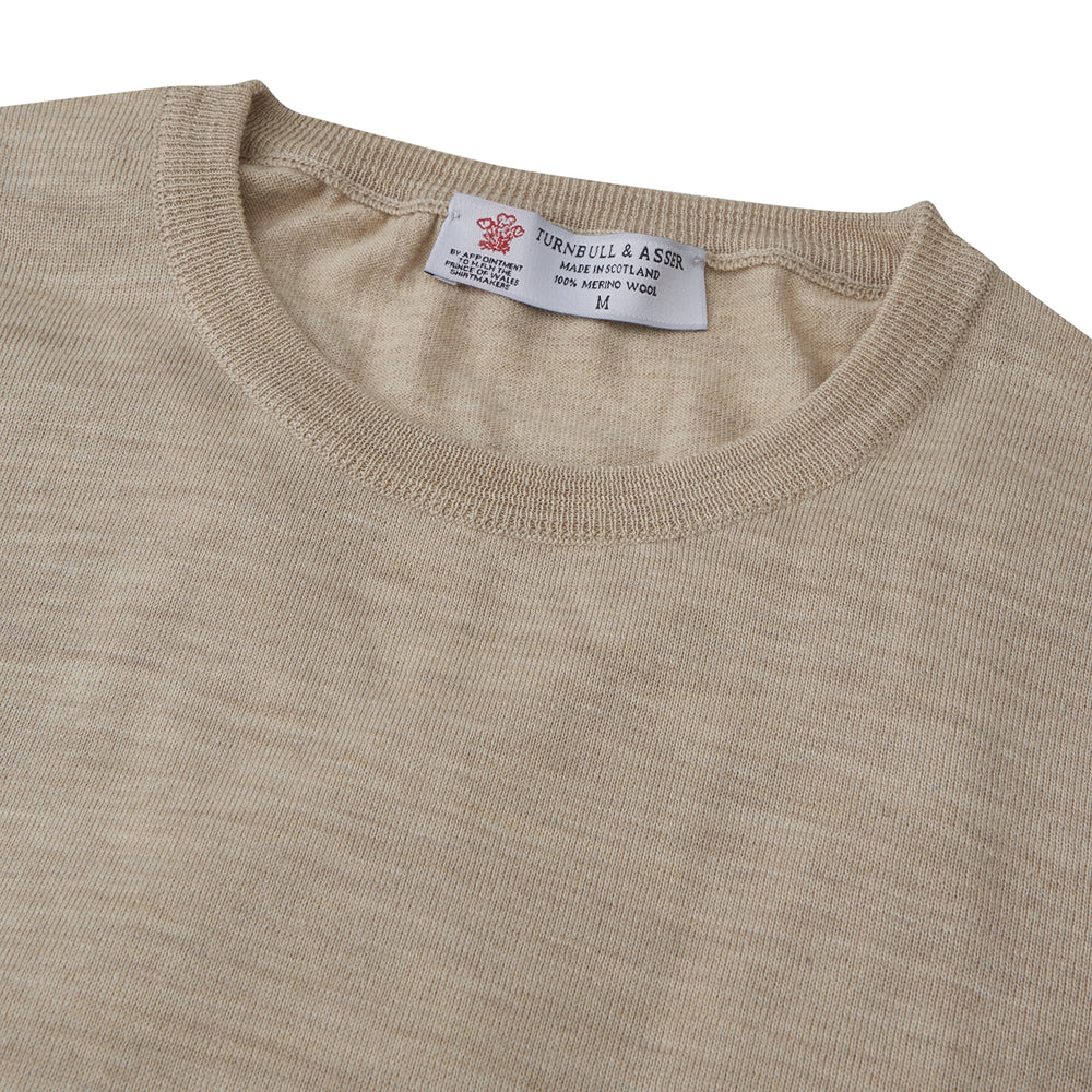 The Camel Fine Merino Crewneck Jumper by Turnbull & Asser is a light brown Scottish knitwear piece with a ribbed collar and cuffs, neatly displayed on a plain white background.