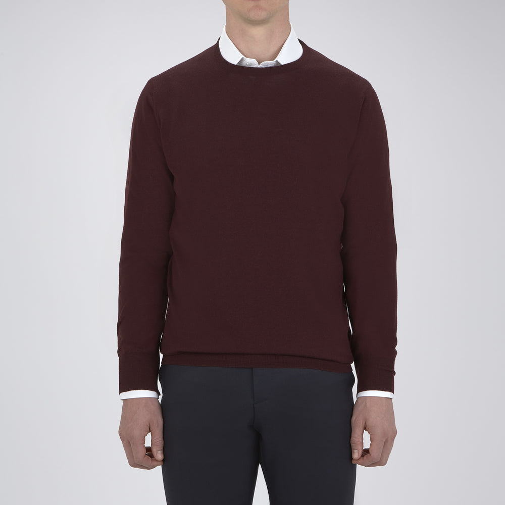 The Turnbull & Asser Wine Crew Neck Merino Wool Jumper, featuring ribbed cuffs and a classic design, is neatly folded on a white background.
