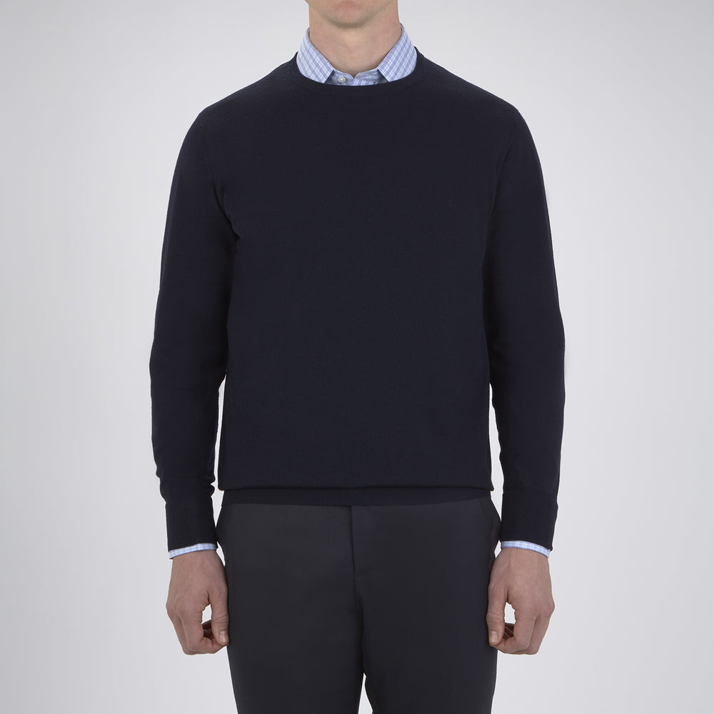 A neatly folded Indigo Crew Neck Merino Wool Jumper by Turnbull & Asser, featuring a visible brand label at the collar and one sleeve tucked across the front, displayed on a white background—a versatile staple for any gentleman's wardrobe.