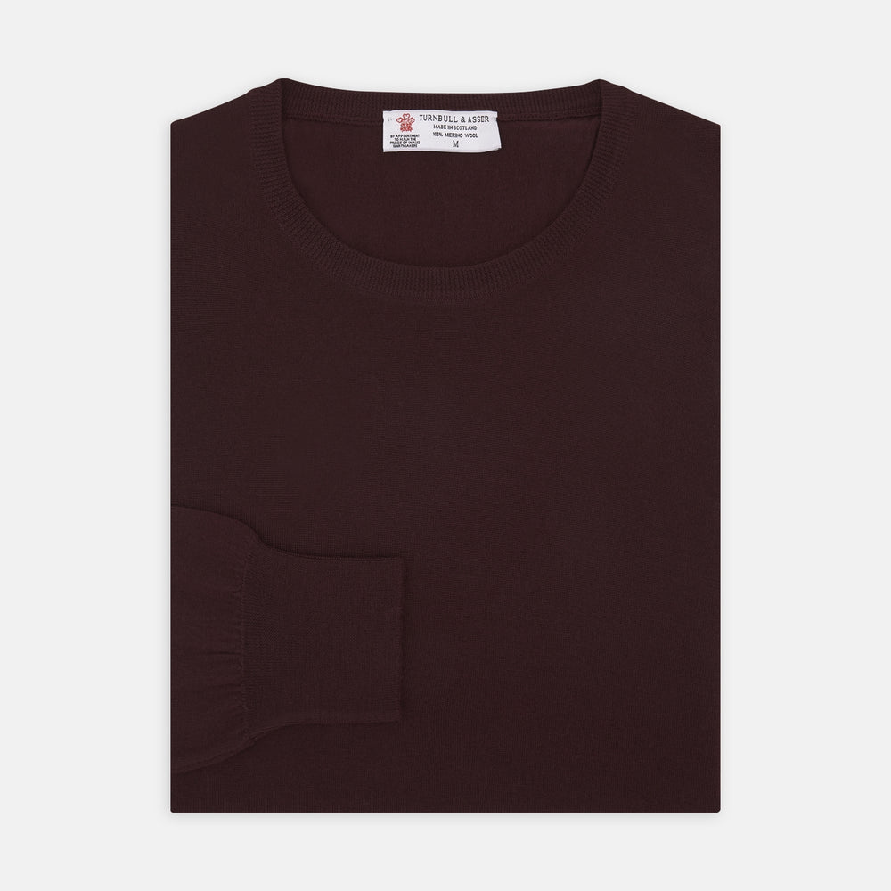 The Turnbull & Asser Wine Crew Neck Merino Wool Jumper, featuring ribbed cuffs and a classic design, is neatly folded on a white background.