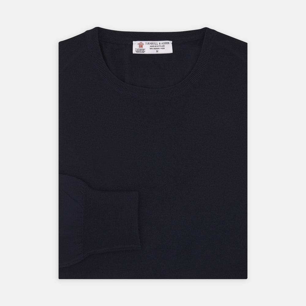 A neatly folded Indigo Crew Neck Merino Wool Jumper by Turnbull & Asser, featuring a visible brand label at the collar and one sleeve tucked across the front, displayed on a white background—a versatile staple for any gentleman's wardrobe.