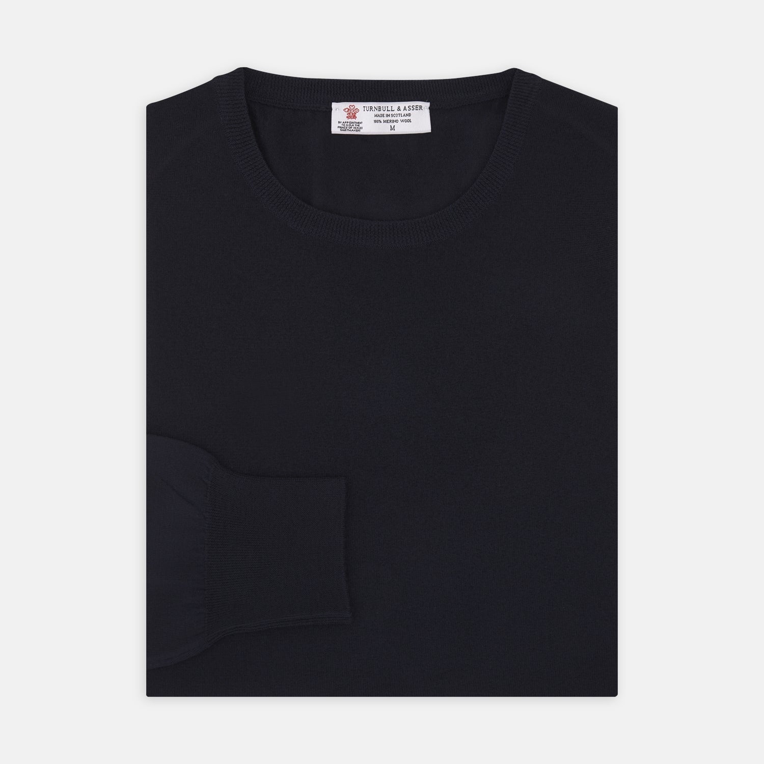 View 1 of product A neatly folded Indigo Crew Neck Merino Wool Jumper by Turnbull & Asser, featuring a visible brand label at the collar and one sleeve tucked across the front, displayed on a white background—a versatile staple for any gentleman's wardrobe.