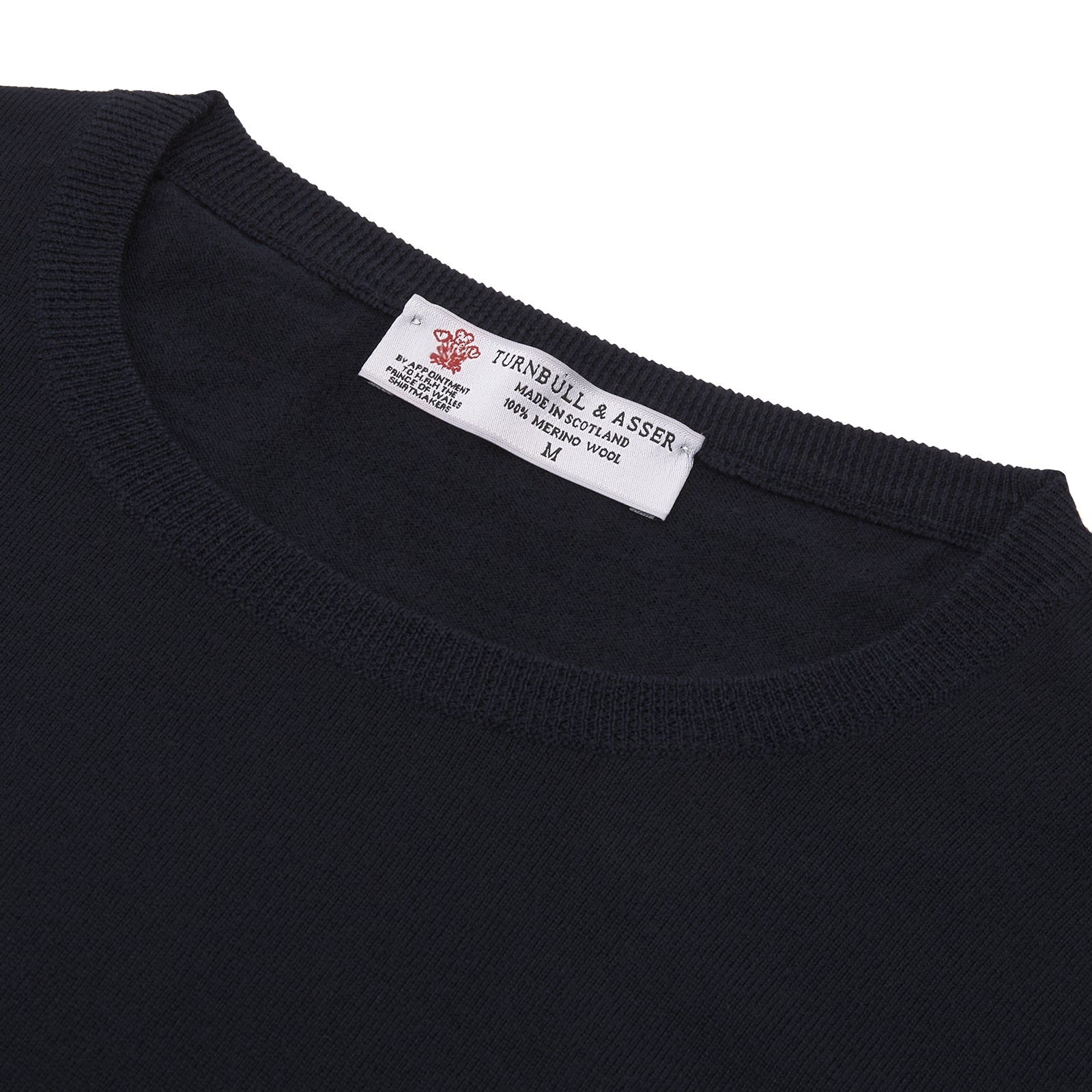 View 4 of product A neatly folded Indigo Crew Neck Merino Wool Jumper by Turnbull & Asser, featuring a visible brand label at the collar and one sleeve tucked across the front, displayed on a white background—a versatile staple for any gentleman's wardrobe.