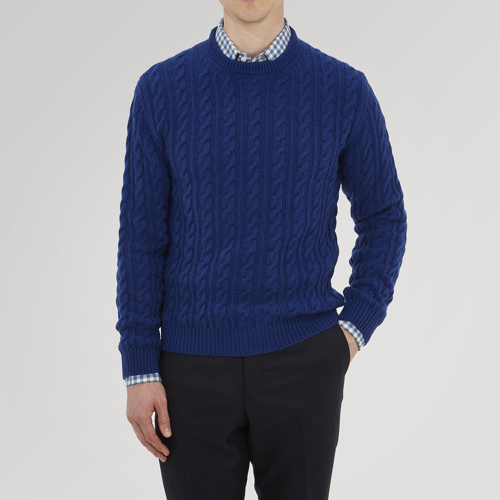 The Blue Crew Neck Cable Knit Cashmere Jumper by Turnbull & Asser features a chunky cable knit, ribbed crew neck and cuffs, and a visible label inside the collar.