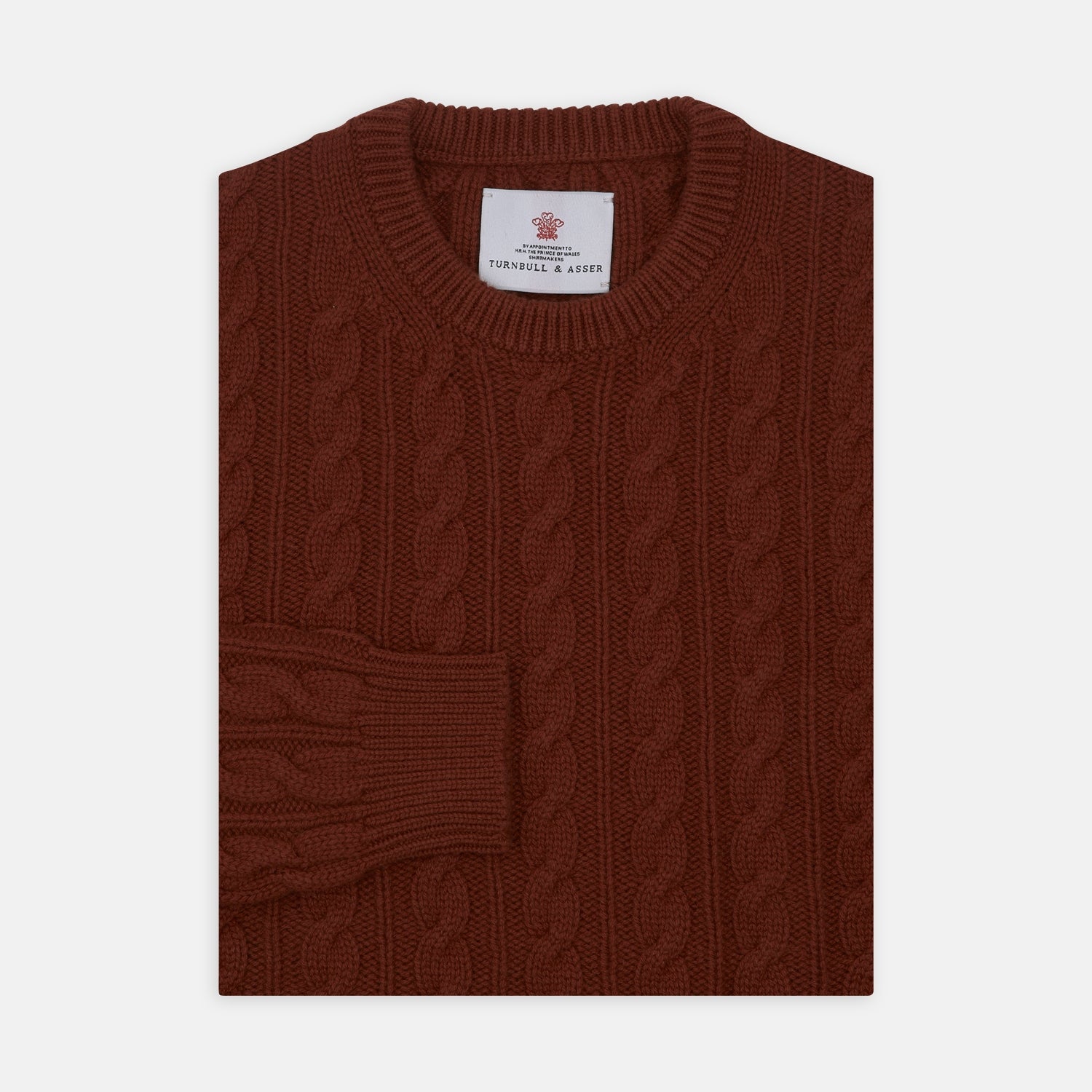 View 1 of product The Harissa Crew Neck Cable Knit Cashmere Jumper by Turnbull & Asser features a chunky, folded cable knit in deep harissa, with ribbed crew neckline and cuffs, and a signature label on the inside collar.