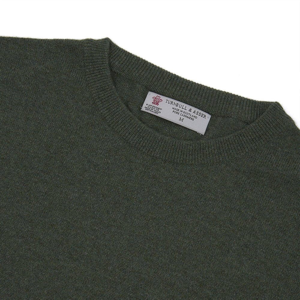 The Turnbull & Asser Green Crew Neck Cashmere Jumper, crafted from luxurious Scottish cashmere with ribbed cuffs, is neatly folded and displayed on a plain white background with the brand label visible inside the neckline.