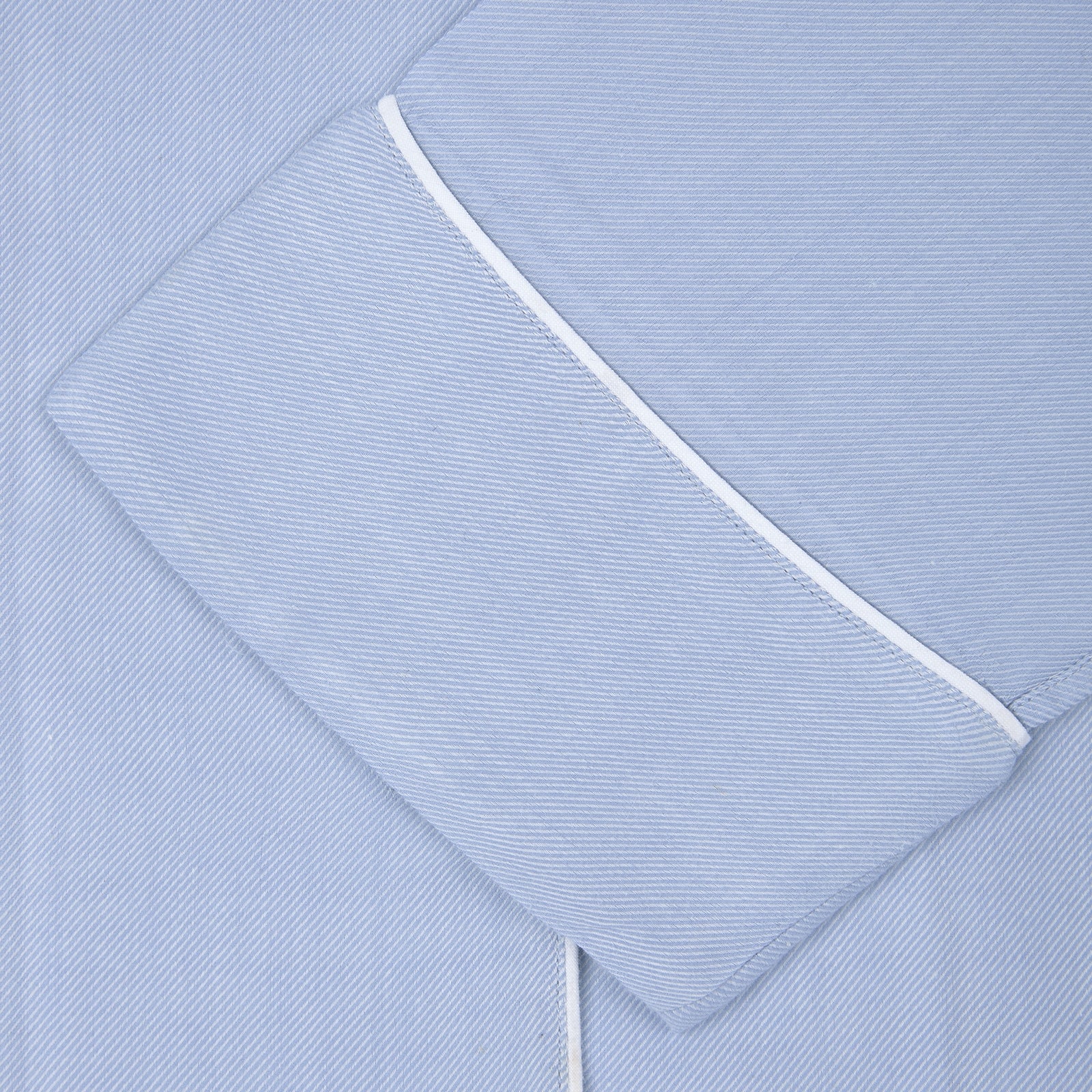 View 2 of product Turnbull & Asser Ladies' Blue Cotton-Cashmere Pyjama Set with white piping features a collared button-up top, neatly folded, and matching drawstring pants laid flat on a plain white background.