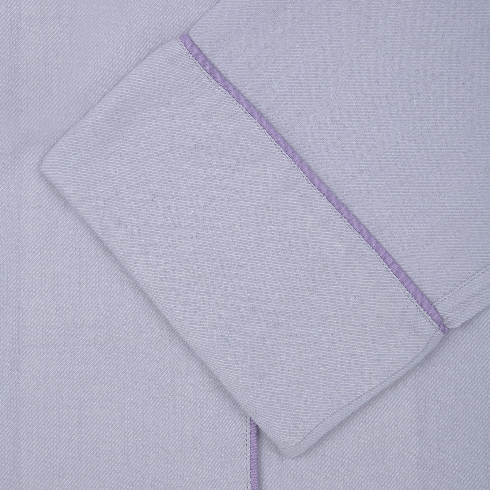 View 2 of product The Ladies' Lilac Cotton-Cashmere Pyjama Set by Turnbull & Asser, with purple piping, collared button-up top featuring a chest pocket, and matching drawstring bottoms, is folded and displayed on a white background.