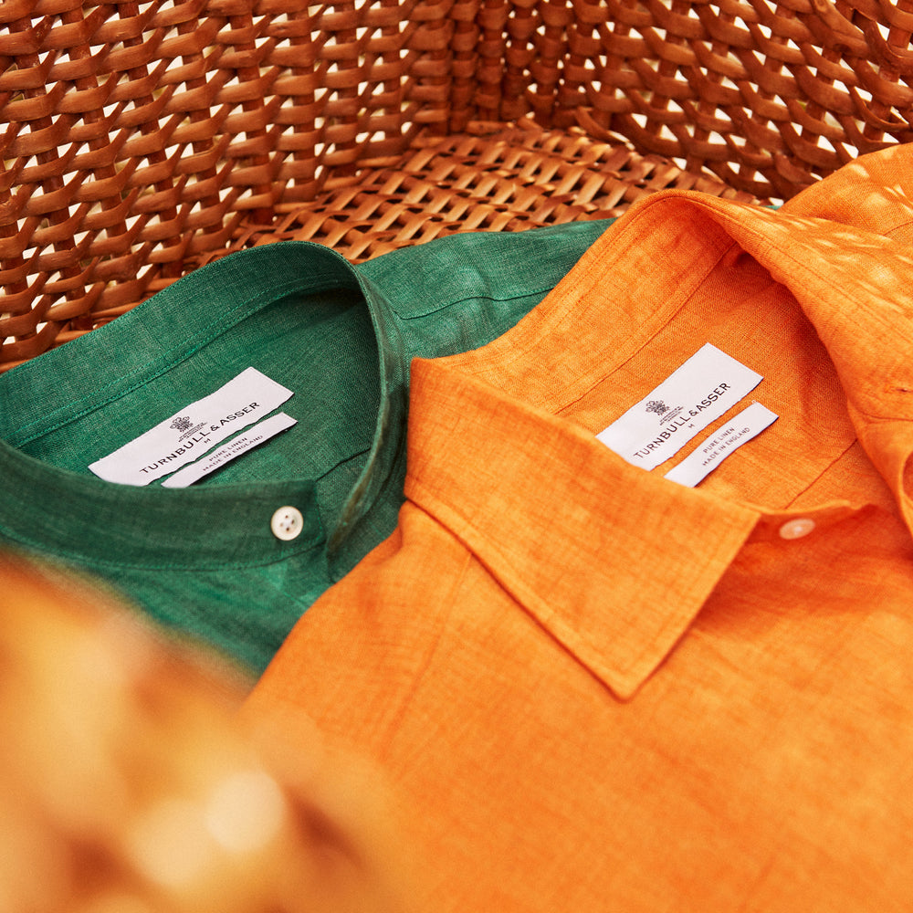 The Turnbull & Asser Orange Weekend Fit Long Sleeve Linen Shirt features a Derby collar, 1-button cuffs, white buttons, and a relaxed fit, shown against a white background.